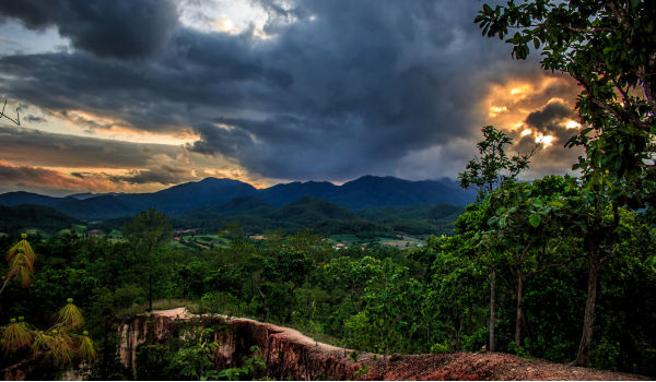 Coucher de soleil sur des montagnes verdoyantes et un canyon, ciel dramatiquement nuageux, ambiance paisible.