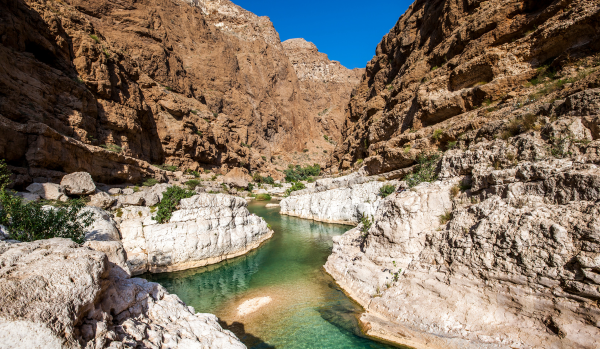 Canyon désertique aux parois rocheuses escarpées, traversé par une rivière turquoise sous un ciel bleu clair.